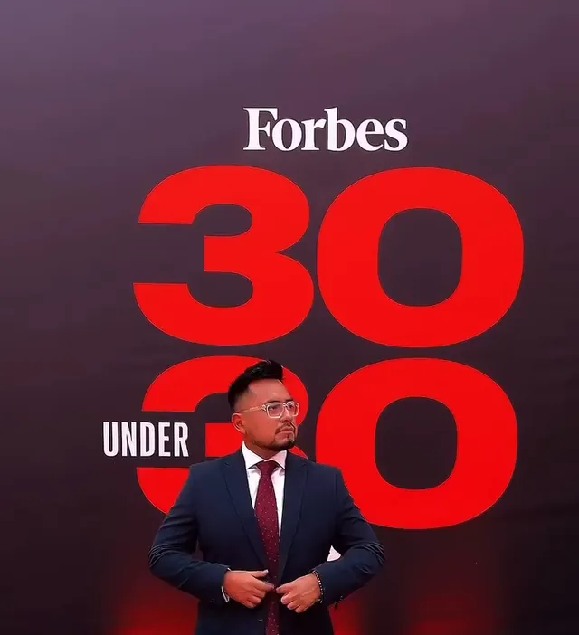 Macuto posa con traje azul y corbata granate en la alfombra roja del Forbes 30 Under 30 de 2024