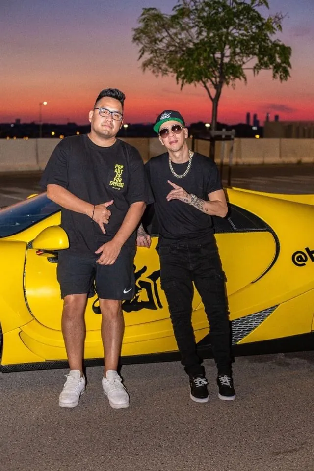 Macuto con Baby Rasta junto a un deportivo amarillo al atardecer