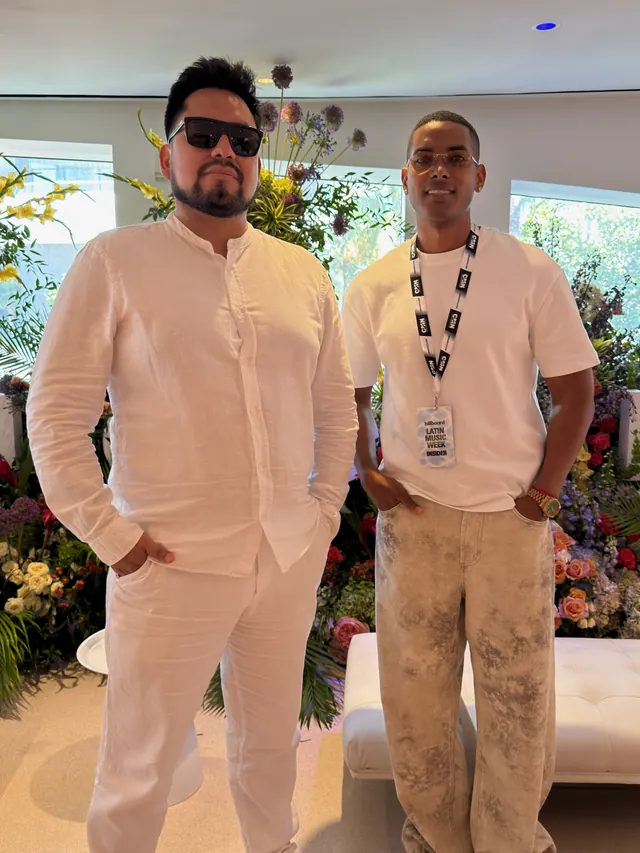 Macuto, vestido de blanco y con gafas de sol, con otro asistente acreditado entre flores